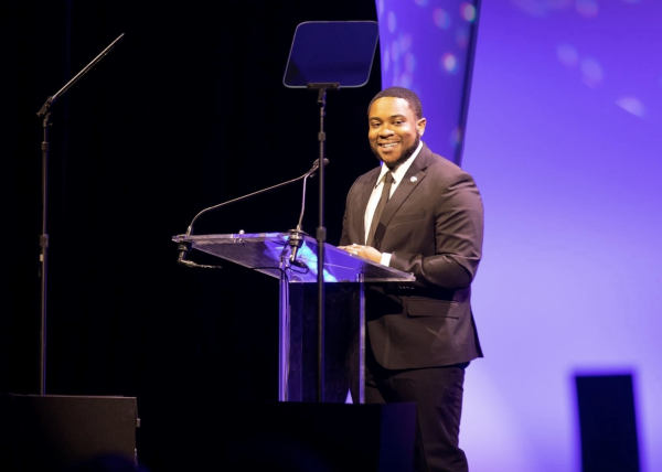 2018 Youth of the Year winner Malachi Haynes stands at a podium giving a speech at the Boys and Girls Club of Metro Denver's 2023 Youth of the Year gala.