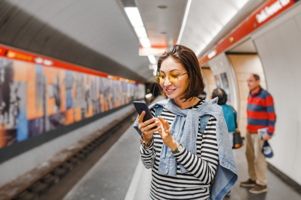 Woman stands with mobile phone in a station for public transportation.